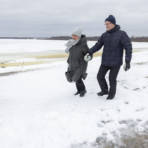 Nainen ja mies kävelevät lumisella rannalla.