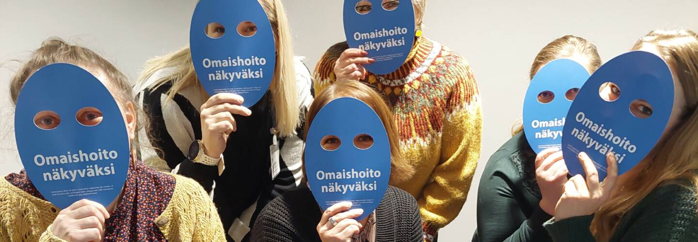 viisi henkilöä paperiset maskit naamojen edessä, joissa lukee omaishoito näkyväksi.